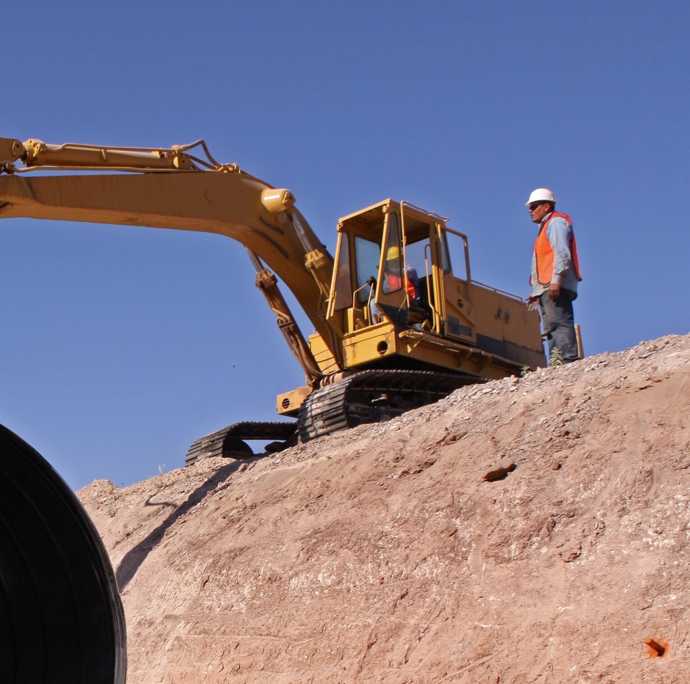 Excavator grading a slope with a spotter watching from above